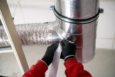 Person sealing ductwork with tape in a ventilation system.