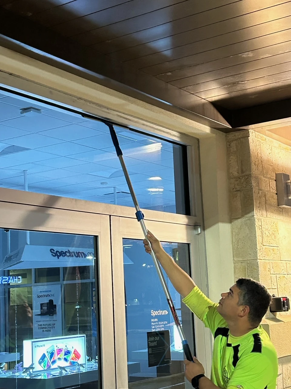A worker cleaning a storefront window with a reacher tool.