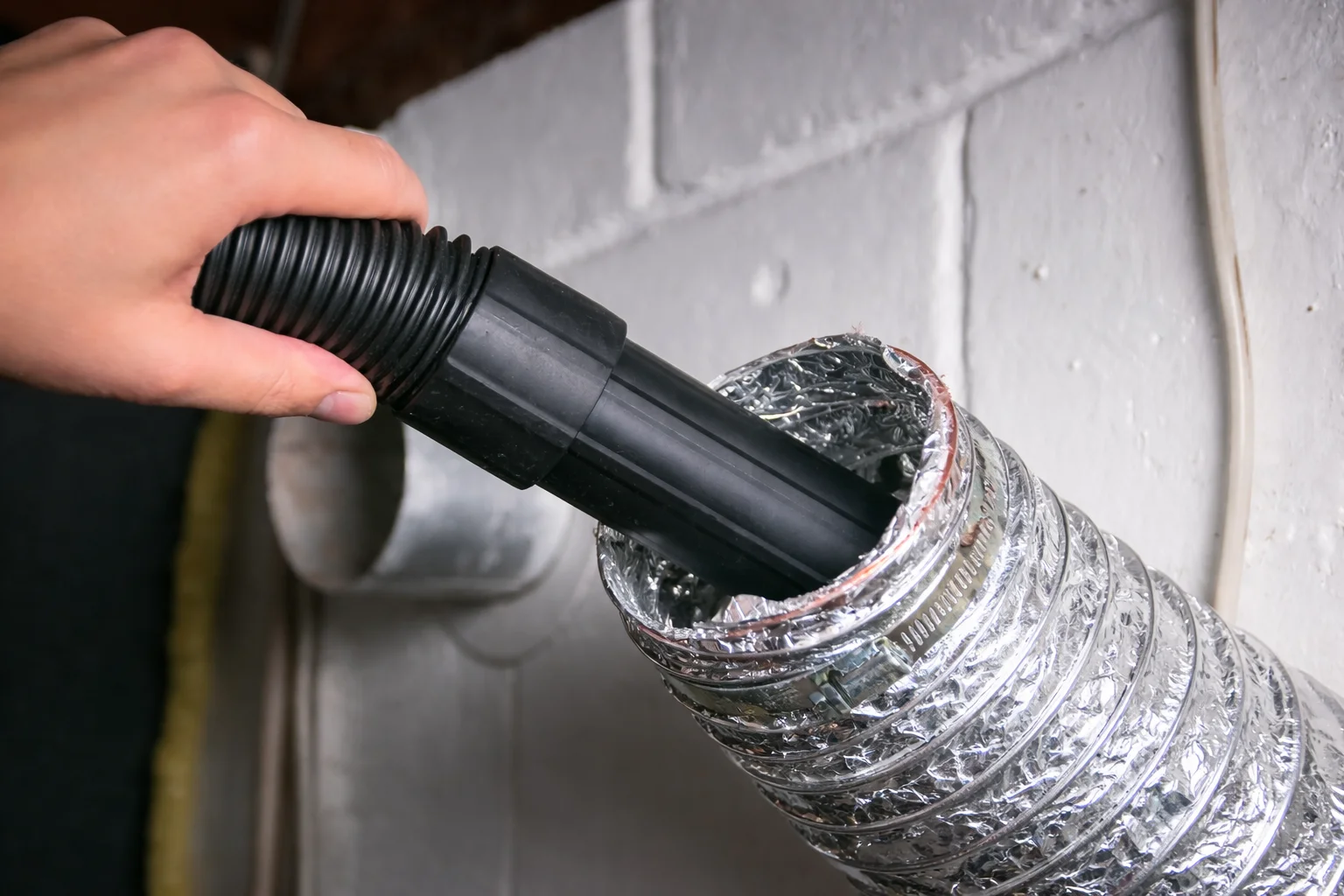 A person using a vacuum hose on metal ducting.